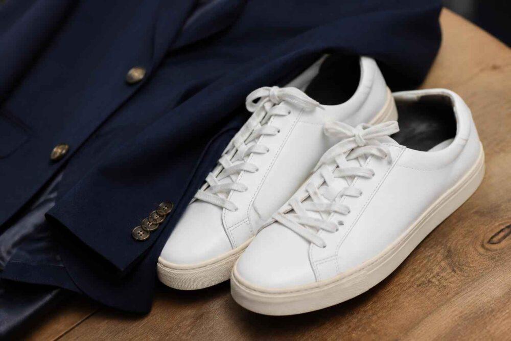 Białe skórzane sneakersy ułożone obok granatowej marynarki na drewnianym stole