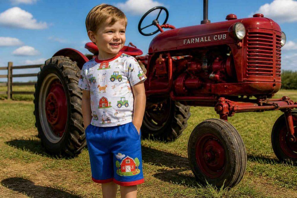 Chłopiec w kolorowych ubraniach stoi przed czerwonym traktorem Farmall Cub na wiejskiej łące