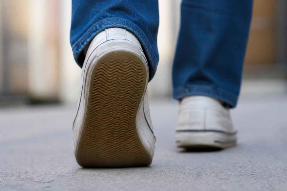 Marsz po miejskim chodniku Zbliżenie na podeszwy białych sneakersów osoby idącej po chodniku w niebieskich spodniach